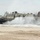 170614-N-PF515-012 A U.S. Navy Landing Craft Air Cushion (LCAC-86) is approaching or landing on a sandy beach, generating significant spray and mist from its air cushion propulsion system. The hovercraft displays clear military markings including 'LCAC-86', 'U.S. NAVY', and an American flag on its hull. The overcast sky and churning water suggest active operational conditions during an amphibious landing exercise or operation.