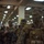 170614-N-GG458-042 A group of military personnel, likely U.S. Marines, are assembled in what appears to be the interior deck of a naval vessel or large military facility. The soldiers are wearing camouflage uniforms, tactical vests, and have green and brown face paint applied. They appear to be staged and ready for a combat operation or amphibious assault exercise.
