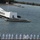 170613-N-HX806-079 The image shows U.S. Navy sailors in dress white uniforms standing at attention on the deck of a naval vessel, facing the USS Arizona Memorial at Pearl Harbor, Hawaii. The iconic white memorial structure is visible floating above the sunken battleship USS Arizona in the harbor. An American flag flies above the memorial, and the surrounding harbor waters and shoreline vegetation are visible in the background.