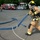 170615-N-YD204-022 A firefighter in full personal protective equipment, including a yellow helmet and SCBA (self-contained breathing apparatus), is pulling a blue fire hose across a paved parking area. In the background, a red fire engine is parked with at least one other firefighter visible near it. The scene appears to be a training exercise or drill conducted in a facility parking lot.