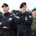 170614-N-PF515-004 The image shows several military personnel in uniform, likely Polish armed forces, standing outdoors in front of coniferous trees. Two men in dark navy uniforms with black berets bearing eagle insignia are prominently featured in the foreground, both with arms crossed. A third individual in camouflage uniform with a green beret is visible in the background right.