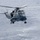 Sterett-Dewey Surface Action Group Deployment A military helicopter is hovering at low altitude over open ocean water. The aircraft appears to be a Sikorsky Sea King or similar naval helicopter, painted in grey military livery with visible identification numbers on the fuselage. The rotor wash is visibly disturbing the water surface below the aircraft.