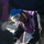 170614-N-XK398-112 A worker wearing a blue hard hat and safety goggles pushed up on their forehead is handling a glass bottle containing a yellow-green liquid. The individual is dressed in a purple safety vest over a dark jacket, suggesting an industrial or maritime work environment. The scene appears to involve liquid sampling or chemical handling procedures.