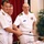Commander, Amphibious Force 7th Fleet, Capt. Matthew Paradise, and Commanding Officer of U.S. 7th Fleet flagship USS Blue Ridge (LCC 19) cut the ceremonial cake at Blue Ridge's change of command reception. Three U.S. Navy officers in white dress uniforms are participating in a ceremonial cake-cutting using a sword. Two officers are jointly holding the sword over a decorated cake, while a third officer stands nearby smiling. The setting appears to be an indoor military ceremony or celebration.