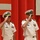 Commander, Amphibious Force 7th Fleet and Blue Ridge Commanding Officer at Blue Ridge's change of command ceremony. Two U.S. Navy officers in white service dress uniforms are simultaneously rendering a salute during what appears to be a formal military ceremony. Both wear white combination covers with gold insignia and display multiple service ribbons and medals on their uniforms. The red curtain backdrop and formal staging suggest this is a change of command or similar official naval ceremony.
