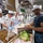 Sterett-Dewey Surface Action Group Deployment A group of military personnel in a ship's galley kitchen are engaged in food preparation. Several individuals wearing white uniforms and white chef's caps with blue latex gloves appear to be assembling food items, while two individuals in Navy blue uniforms observe. The setting appears to be a collaborative cooking or culinary exchange between different naval forces.