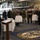 170614-N-JI086-354 A military briefing or reception is taking place in what appears to be a ship's hangar bay, with a uniformed officer speaking at a wooden podium to a group of multinational military personnel. A decorative rug bearing a U.S. Navy ship's seal/crest is visible in the foreground. The setting and attire suggest a formal multinational military gathering, likely aboard a U.S. Navy vessel.