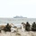 170614-N-PF515-003 Four soldiers in camouflage uniforms are positioned behind a sandbag fortification on a sandy beach, facing the sea. They appear to be in a defensive or observation posture, with at least one soldier visibly holding a weapon. A large naval vessel, likely an amphibious warship, is visible in the background on the water.