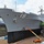 USS Blue Ridge Sailors give the ship a new coat of paint A large gray naval vessel bearing hull number '19' is undergoing maintenance in a dry dock facility. The ship is elevated out of the water, exposing its dark-painted hull bottom, with workers using aerial lift equipment to perform work on the hull surface. The setting appears to be a shipyard, likely in Japan based on the surrounding infrastructure and vegetation.