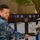 NMCSD NEC Fair A U.S. Navy sailor in digital camouflage (NWU Type I) is presenting an informational display board about 'Biomedical Equipment Tech' to another person, also in military uniform. The display board features colorful lettering, a medical/biomedical insignia patch, and several printed documents including what appears to be a USMAP document. The setting appears to be an outdoor or semi-covered area, likely during a career or recruiting fair.