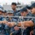 Sterett-Dewey Surface Action Group Deployment The image shows U.S. Navy sailors and what appear to be Chinese People's Liberation Army Navy (PLAN) personnel engaged in a joint rope-tying or knot-work training exercise. The two groups, identifiable by their distinct camouflage uniforms, are collaborating closely around a horizontal metal bar with white ropes. A naval vessel is visible in the background, suggesting this takes place at a port or aboard a ship.