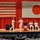 Commander, Amphibious Force 7th Fleet greets Capt. Paradise at Blue Ridge's change of command ceremony. A formal military ceremony is taking place on a stage with the flags of the United States and Japan displayed prominently on a red curtain backdrop. Two naval officers in white dress uniforms are shaking hands near a podium, while two other officers are seated on stage. An audience of uniformed personnel observes from the foreground.