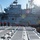 170614-N-XK398-038 A naval deck scene showing sailors in safety gear performing line-handling or mooring operations alongside a large amphibious assault ship marked with the hull number '6'. Personnel are wearing red life vests and blue hard hats, with one individual in a white shirt labeled 'CHAPLAIN' visible on the right. The foreground shows a non-skid flight deck surface with tie-down fittings, suggesting this photo is taken from the deck of another vessel.