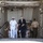 170613-N-FM530-059 The image shows a group of individuals walking through what appears to be the interior bay or hangar deck of a naval vessel. The group includes a senior U.S. Navy officer in dress whites, a civilian in a dark suit with a gold tie, and a U.S. Marine in service uniform. Additional military personnel in white uniforms are visible in the background.