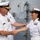 Sterett-Dewey Surface Action Group Deployment Two naval officers in white dress uniforms are shaking hands in what appears to be a formal greeting or ceremony aboard or near a naval vessel. The male officer on the left has his hand on the female officer's shoulder while shaking her hand, suggesting a senior-to-junior or peer greeting. A third sailor in white uniform is visible in the background.