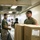 170609-N-FM530-031 Military personnel in olive green t-shirts and camouflage trousers are working in what appears to be a ship's cargo or supply corridor. They are handling cardboard boxes along a conveyor belt system in a confined, industrial interior space. Multiple service members are visible working together in a logistics or resupply operation.