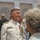 Marine Barracks Washington; EveningParade July 14, 2017 A senior military officer in white dress uniform adorned with numerous medals and ribbons is engaged in conversation at what appears to be a formal military ceremony or reception. The officer is smiling and interacting with civilians, including an elderly couple in the foreground. The setting appears to be an elegant indoor venue with arched architectural details.