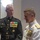 Marine Barracks Washington; EveningParade July 14, 2017 Two senior U.S. military officers in formal dress uniforms are engaged in conversation. The officer on the left wears a U.S. Marine Corps dress blue uniform with a sword belt and multiple ribbons and medals, while the officer on the right wears a U.S. Navy white dress uniform adorned with an extensive array of medals and decorations. Both appear to be of high rank based on the volume and variety of their awards.