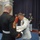 Marine Barracks Washington; EveningParade July 14, 2017 A formal military ceremony is taking place indoors, likely at a U.S. Marine Corps event. A senior officer in white dress uniform is presenting or receiving a document/award to/from a Marine in dress blues. Additional uniformed personnel, including ceremonial guards and a general officer, are present in the background.