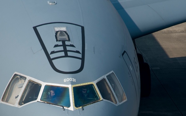 A close-up frontal view of a U.S. Air Force C-17 Globemaster III military transport aircraft on a tarmac. The aircraft's nose section is prominently featured, showing the cockpit windows with crew members visible inside. The serial number 60031 is visible below the cockpit, and a unit insignia shield is displayed on the fuselage.