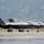 Two F-35A Lightning II stealth fighter jets are taxiing on a runway apron, both bearing the 'HL' tail code indicating assignment to Hill Air Force Base, Utah. The aircraft display serial numbers including '5101' and appear to be in a standard gray stealth finish with canopies closed. A mountainous terrain consistent with the Wasatch Range is visible in the background.