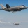 A U.S. Air Force F-35A Lightning II stealth fighter jet is captured in flight releasing a munition, identifiable as a GBU-31 JDAM (Joint Direct Attack Munition). The aircraft bears the 'HL' tail code, indicating assignment to Hill Air Force Base, Utah. The image is a high-quality aerial photograph taken against a clear blue sky with scattered clouds below.