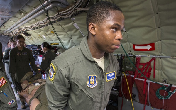 The image shows U.S. Air Force personnel conducting aeromedical evacuation operations inside a military transport aircraft. Multiple crew members in olive green flight suits are attending to a patient on a litter/stretcher. Medical equipment and supplies are visible throughout the aircraft interior.