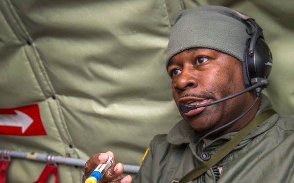 A U.S. Air Force Technical Sergeant named Khary A. Hunt is pictured inside what appears to be a military aircraft, wearing a flight suit and communications headset. He is handling medical syringes and vials, suggesting he is performing or preparing for aeromedical duties. The American flag patch and master flight nurse/aircrew badge are visible on his uniform.