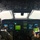 Two flight crew members are seated in the cockpit of a military aircraft, likely a WC-130 or similar reconnaissance/weather aircraft, flying through dense cloud cover or a storm system. The cockpit features a modern glass avionics suite with multiple multifunction displays, and the right-seat pilot is holding a tablet displaying weather radar imagery. The exterior visibility is near-zero, suggesting flight through clouds or a weather system.