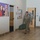 Hurricane Harvey Response A U.S. Army soldier in camouflage uniform (OCP/MultiCam pattern) is walking through an indoor hallway of what appears to be a military facility or barracks. The soldier is carrying a large green duffel bag in one hand and wearing a heavy rucksack on their back, suggesting they are arriving or departing. A promotional poster featuring a military family is visible on the wall to the left.