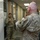 Hurricane Harvey Response Military personnel in OCP (Operational Camouflage Pattern) uniforms are gathered in what appears to be an operations or planning center. A soldier on the left is briefing or presenting information to colleagues, gesturing toward documents and maps posted on a whiteboard. The setting suggests a military staff planning or operations review session.
