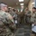 Hurricane Harvey Response A group of U.S. Army soldiers in Operational Camouflage Pattern (OCP) and Army Combat Uniform (ACU) uniforms are gathered in what appears to be an office or administrative facility. A soldier on the right side appears to be briefing or instructing the group, holding papers and gesturing. The setting suggests a training visit, inspection, or operational briefing in an indoor military or government office environment.