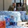 Military personnel in uniform are organizing and distributing large quantities of bottled water and supplies outside a building. The scene appears to be a disaster relief or emergency supply distribution operation, with pallets of Nestlé Pure Life water cases stacked prominently. At least four service members are actively handling and arranging the supplies.