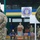 A military ceremony for Exercise Rapid Trident 2017, a multinational military exercise focused on partnership, security, and assurance. A uniformed officer is speaking at a podium bearing the Ukrainian trident emblem, with the official Rapid Trident 2017 sign visible in the background. Multiple military personnel from various nations are present on and around a stage decorated with Ukrainian blue and yellow colors.