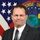 Terrence McCall A formal official portrait of a middle-aged man wearing a dark gray suit, white dress shirt, and patterned tie. He is posed in front of a U.S. flag and what appears to be a Defense Intelligence Agency (DIA) seal/flag. The image is a professional headshot consistent with U.S. government or military civilian official photography.