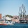 A U.S. Coast Guard patrol boat (hull number 45659) is underway in a harbor, with a large historic tall ship docked at a pier in the background. The scene appears to be in Boston Harbor, as evidenced by the Bunker Hill Monument obelisk visible in the background. The setting includes a waterfront urban area with brick buildings and the tall ship decorated with signal flags.