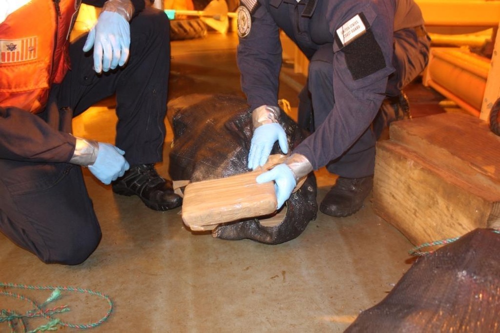 A Coast Guard Cutter Aspen crewmember inspects a bale of cocaine