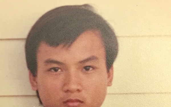 This is an archival identification photograph, consistent with a booking or registration photo. The subject is holding a dark board with handwritten text reading 'NGUYEN MINH KY' and 'M.34474'. The photo appears aged, suggesting it was taken several decades ago.
