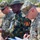 Three military personnel are gathered outdoors, reviewing and writing on documents. Two individuals wear U.S. Army uniforms with OCP (Operational Camouflage Pattern), while the central figure wears a Nigerian Army uniform with distinctive patches and a bush hat. The setting appears to be an outdoor military exercise or joint coordination meeting.
