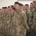 A large formation of military personnel dressed in MultiCam/OCP camouflage uniforms are standing at attention in an indoor facility. The soldiers appear to be participating in a formal military ceremony or formation event. The group includes both male and female service members arranged in multiple rows.