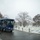 First Snow of the Season at Arlington National Cemetery A dark navy blue Arlington National Cemetery Tours trolley bus travels along a wet road during a light snowfall. The trolley passes rows of white military grave markers dusted with snow, surrounded by bare winter trees. The overcast, snowy conditions create a somber and reverent atmosphere at the historic cemetery.