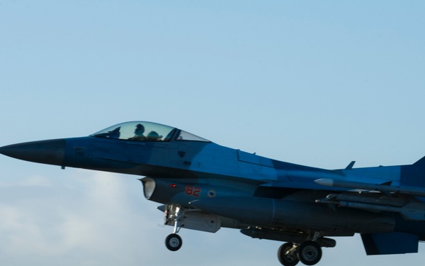 An F-16 Fighting Falcon jet fighter is captured just after takeoff or during landing on a runway, with landing gear still deployed. The aircraft bears the tail code 'AK' and serial number '35400', indicating it belongs to an Alaska-based unit of the United States Air Force. The aircraft appears to be carrying external stores including missiles and fuel tanks.
