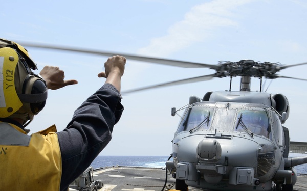 USS Mustin (DDG 89) Sailor signals to HSM 51 Sea Hawk Helicopter during flight quarters