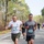 Two lead runners compete in an organized road race on a tree-lined paved road. The foreground runners wear bibs numbered '1' and '220', with several other participants visible in the background. The event appears to be a military or community 5K/fun run based on the bib design referencing 'MCAS Cherry Point, NC'.