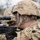 A soldier in full combat gear is aiming an Enhanced Sniper Rifle (Remington Model 700 M24) equipped with a telescopic scope. The soldier is wearing MultiCam/OCP camouflage uniform, a tactical helmet with identifier markings, and has camouflage face paint applied. A second soldier in similar gear is visible in the background.