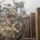 A soldier in full combat gear is seen aiming a rifle while navigating through what appears to be a military training environment with wooden structures. The soldier is equipped with modern tactical gear including a helmet with mounted accessories, ballistic eyewear, and a camouflage uniform. A second soldier in different camouflage pattern is visible in the foreground, out of focus.