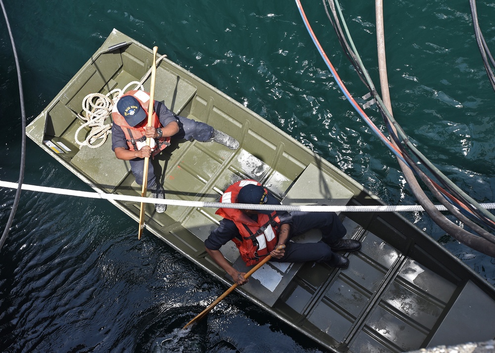 Deck Sailors use a small craft to perform corrosion preventative maintenance on the port side anchor.