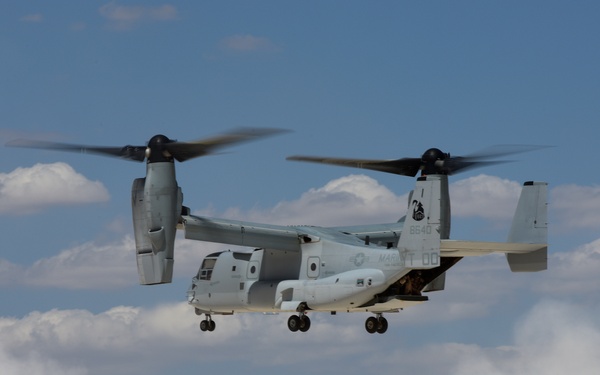 A U.S. Marine Corps MV-22 Osprey tiltrotor aircraft is captured hovering or landing in a desert environment, generating a large dust cloud from its rotor wash. The aircraft's nacelles are in vertical/transitional position, consistent with helicopter-mode flight. Markings and insignia indicate this is a USMC operational aircraft.