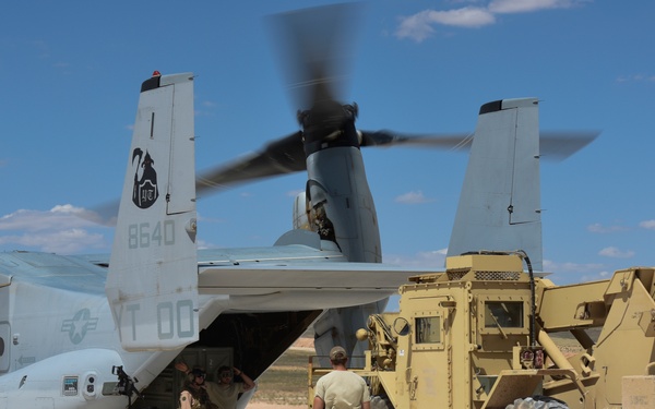 A U.S. Marine Corps MV-22 Osprey tiltrotor aircraft (tail number 8640, squadron markings 'YT 00') is on a desert landing strip with its rear ramp open. Military personnel in tan/coyote uniforms are conducting a loading or unloading operation, assisted by a military-painted Skytrak telescopic forklift. The scene appears to be a forward operating or expeditionary logistics exercise in an arid environment.
