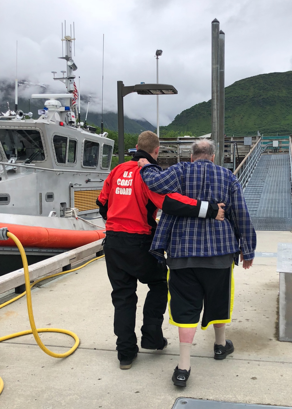A Coast Guard Station Valdez boat crew member assists a 72-year-old man to emergency medical services